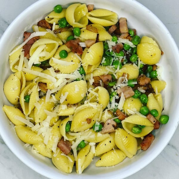 Conchiglie pasta with peas, bacon, and shredded Parmesan cheese in a white bowl.