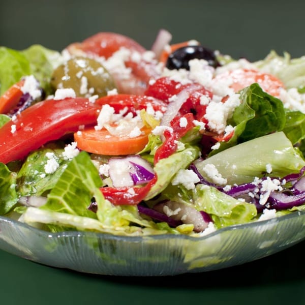 Close-up of a vibrant Italian salad with lettuce, tomatoes, olives, red onion, and feta cheese.