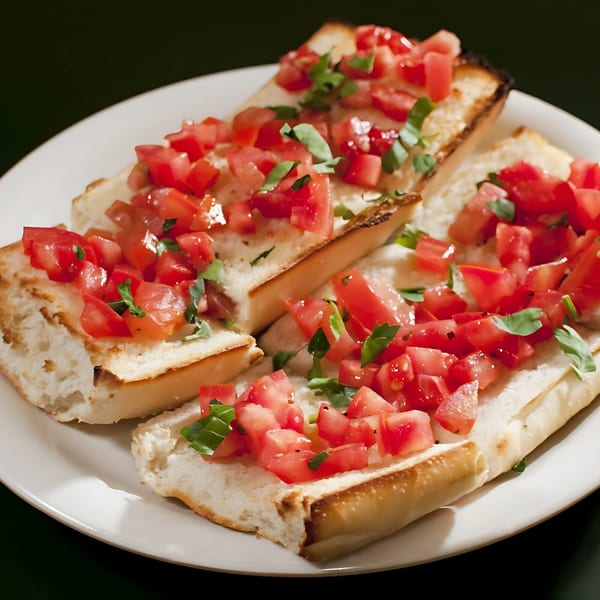 Four pieces of bruschetta topped with diced tomatoes and fresh basil on a white plate.
